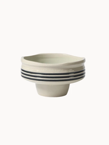 Ceramiczna miska na podwyższeniu w jasnokremowym kolorze, pokryta spękanym szkliwem z trzema czarnymi paskami wokół środka.
